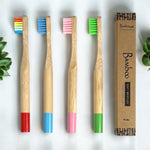 Four bamboo toothbrushes with colored bristles and a cardboard box on a white background.