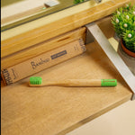 Bamboo toothbrush with green bristles on a wooden tray, next to its packaging.