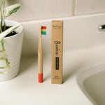 Bamboo toothbrush with rainbow bristles and packaging on a bathroom counter.