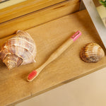Wooden toothbrush with pink bristles on a wooden surface with two shells.