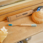 Bamboo toothbrush with packaging on a wooden surface with shells.