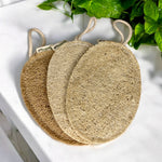 Three natural loofah sponges on a white surface with greenery in the background