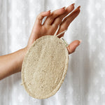 Hand holding a natural loofah pad against a white background