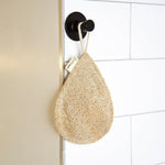 Natural loofah hanging on a black hook against a tiled bathroom wall.