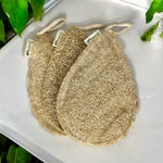 Three natural loofah sponges on a white surface with green leaves in the background.